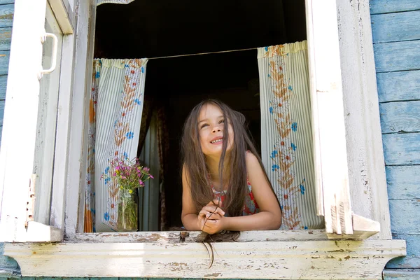 Laughing joyful little girl looking out from the window wide open