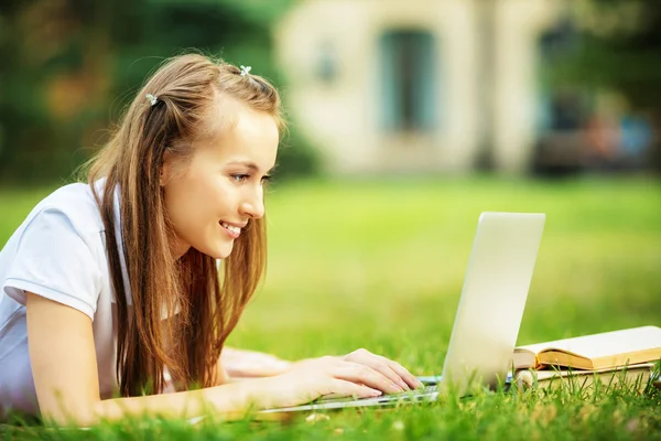 Student woman lying on the grass with  laptop