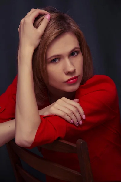 Beautiful young girl sitting on a chair in a red blouse