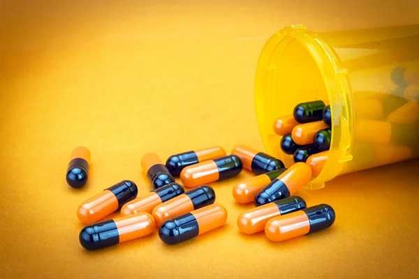 Pills spilling from an open bottle isolated on orange background