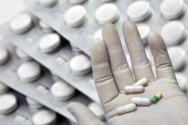 Packages of pills, left hand with white glove of latex with some pills