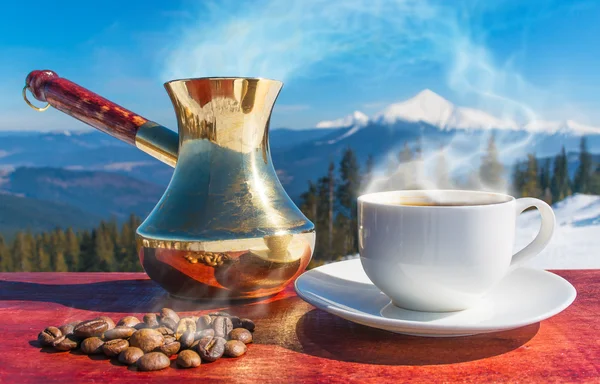 A cup of coffee, coffee beans, coffee mountains in the background.