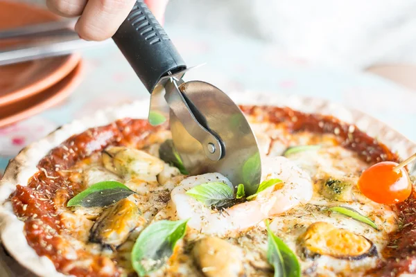 Women hand holding pizza cutter and cutting pizza