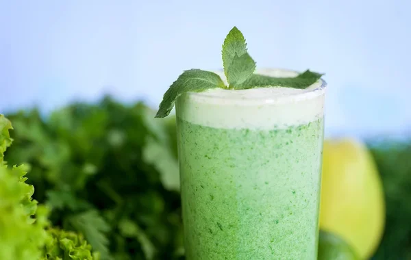 Detox  diet,  healthy food concept. green smoothie in glass and green vegetables on blue wooden desk