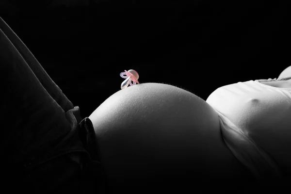Color key of pacifier on pregnant mother belly at black background