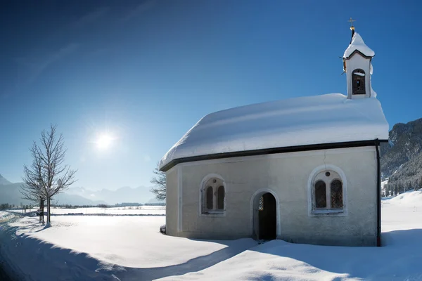 Old chapel in winter snow landscape with sunlight and blue sky