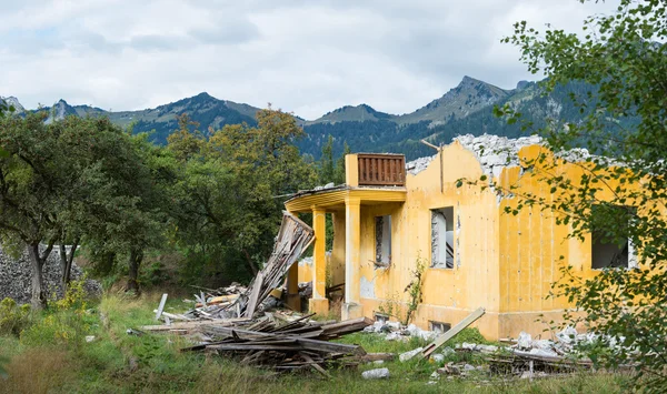 Destroyed old orange house next to trees and mountains