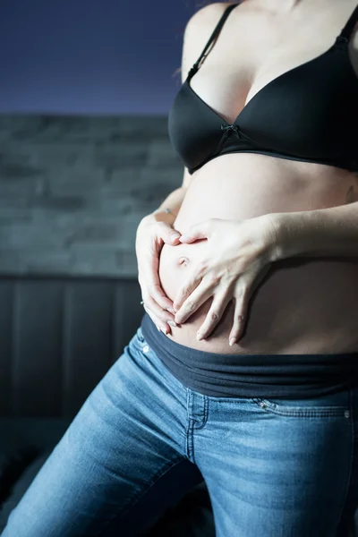 Pregnant woman holding her belly with handy forming a heart