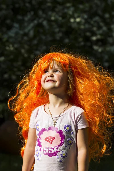 Little girls in brightly colored carnival wigs in the setting sun in summer in the garden