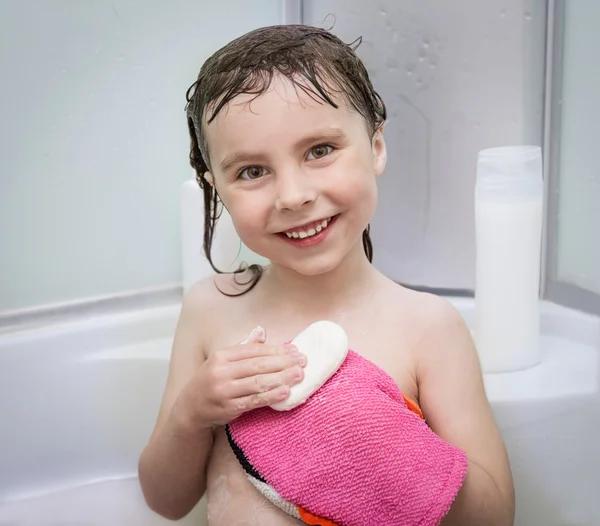 Little smiling girl in the shower with a washcloth and soap