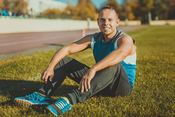 Sporting an attractive man sitting on grass and rests in the stadium