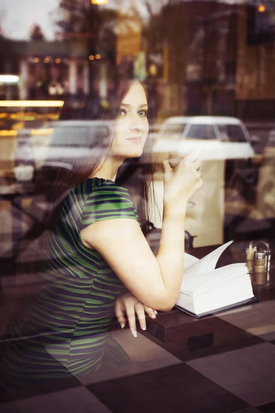 Brunette woman sitting at the cafe reading book, studing and drinking coffee