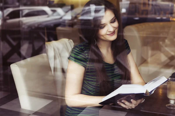 Brunette woman sitting at the cafe reading book, studing and drinking coffee. Copy Space