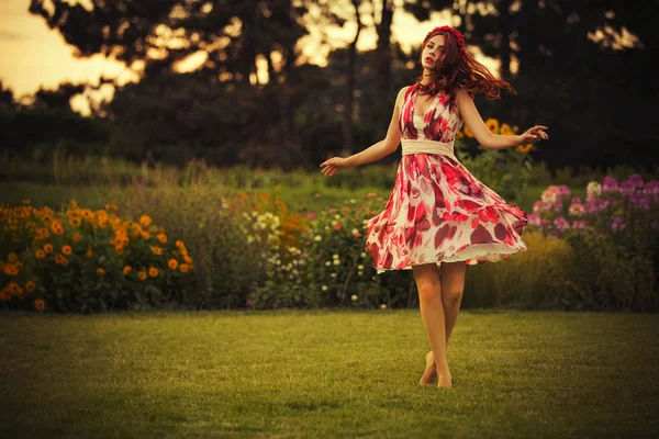 Beautiful brunette caucasian woman in white and red dress at the park in red and yellow flowers on a summer sunset dancing in the meadow. Copy Space