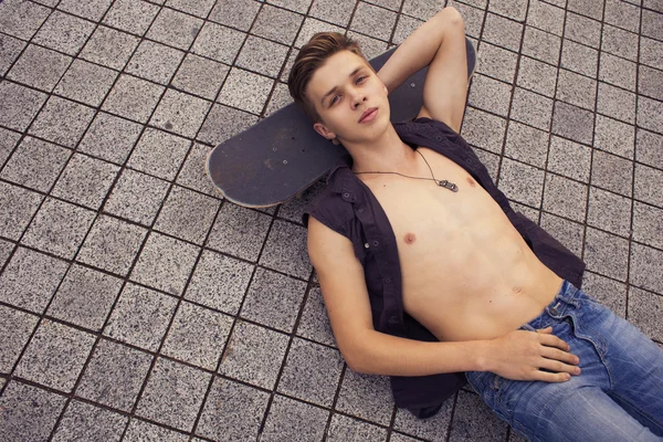 Young blonde guy on skateboard in casual outfit in the urban cit