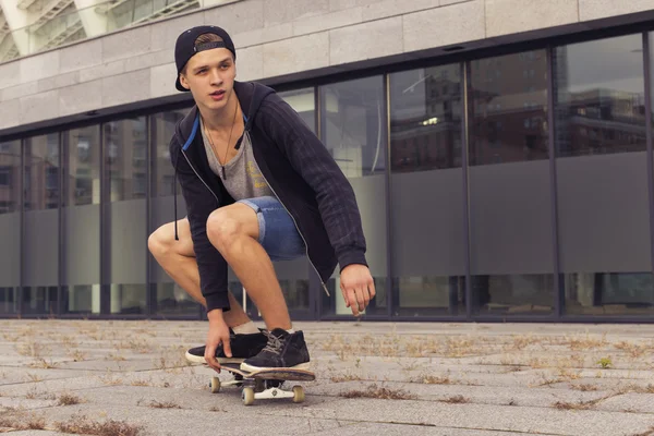 Young blonde guy on skateboard in casual outfit in the urban cit