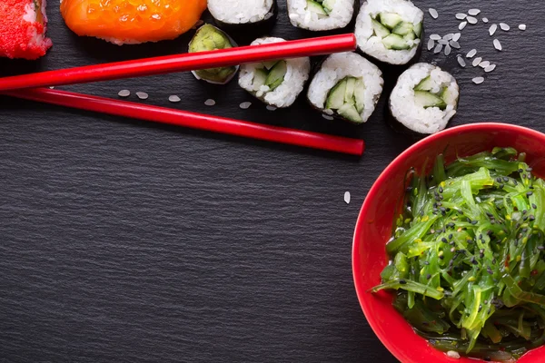 Sushi and green seaweed salad on a slate table