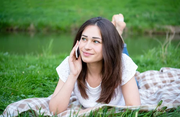 Girl speaks by phone laying on a lawn