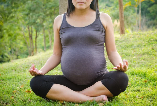 Pregnant woman doing yoga in nature outdoors.