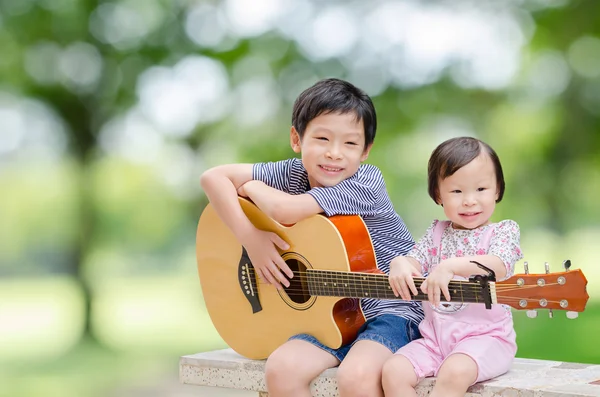 Boy and his sister play guitar and sing in garden