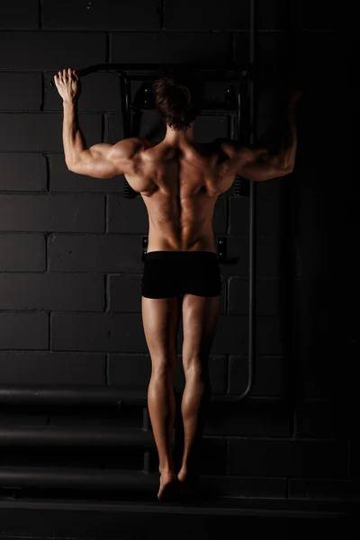 Athlete muscular fitness male model pulling up on horizontal bar