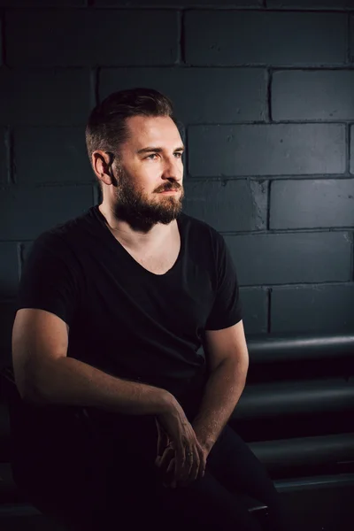 Handsome bearded men in black shirt thinking about his life near brick wall