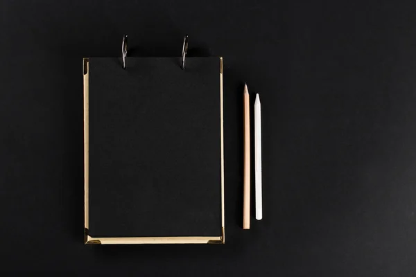 Close notepad with black cover with a pencil on black background