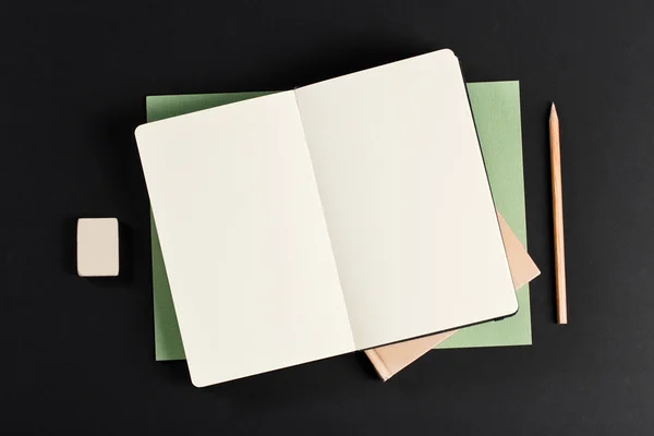 Open blank notepad with empty white pages laying above book with