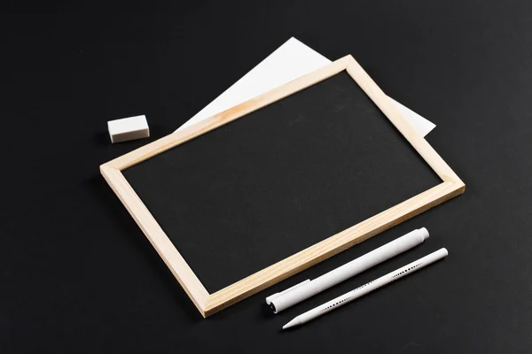 Wooden frame with black field with marker and white pencil and eraser on black paper. Mockup. Real photo for you text
