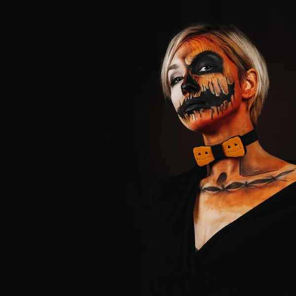 Halloween portrait of body art pumpkin girl with pumpkin bowtie on black background. Real greasepaint and face art makeup. Square photo