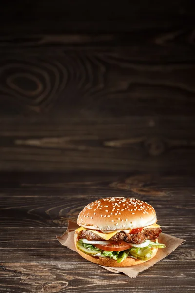 Cheese burger with grilled meat, cheese, tomato, on craft paper on wooden surface. Fast food template.