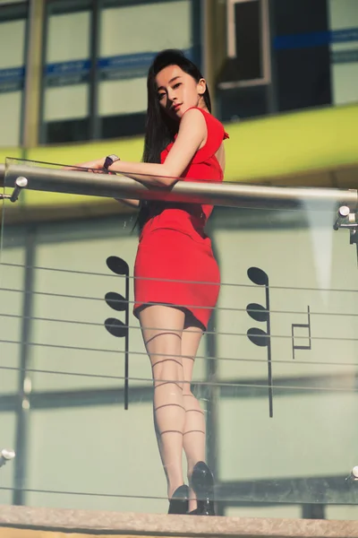 Beautiful Asian girl model in red dress posing at the modern music note style city background.
