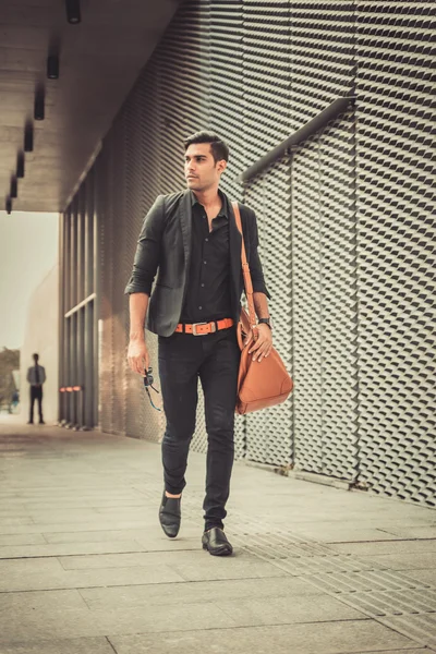 Stylish model looking man profile with handbag on his shoulder in modern architectural environment.