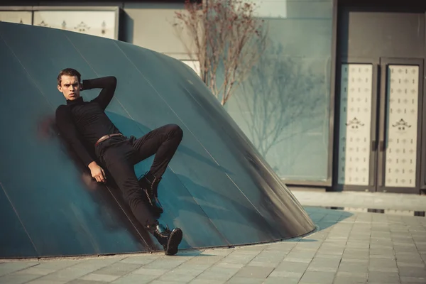 Man model in strict black dress near modern architectural environment.