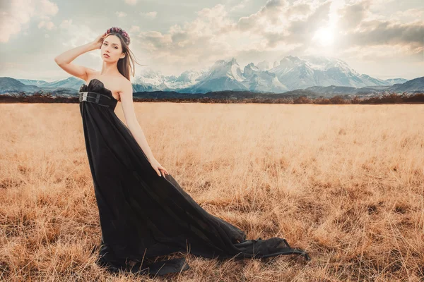 Beautiful girl in a black dress with flowers near mountains
