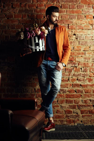 Handsome young man in smart jacket with bouquet of flowers  poses in front of the  wall