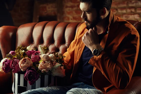 Handsome young man in smart jacket with bouquet of flowers  poses in front of the  wall