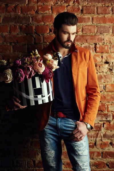 Handsome young man in smart jacket with bouquet of flowers  poses in front of the  wall