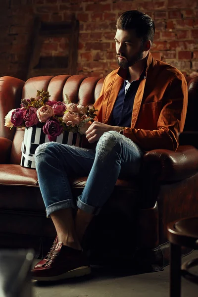 Handsome young man in smart jacket with bouquet of flowers  poses in front of the  wall