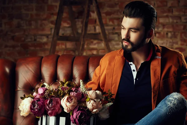 Handsome young man in smart jacket with bouquet of flowers  poses in front of the  wall