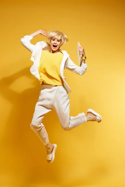 Young girl having fun and jumping. Smiling girl with yellow background wearing fashion clothes