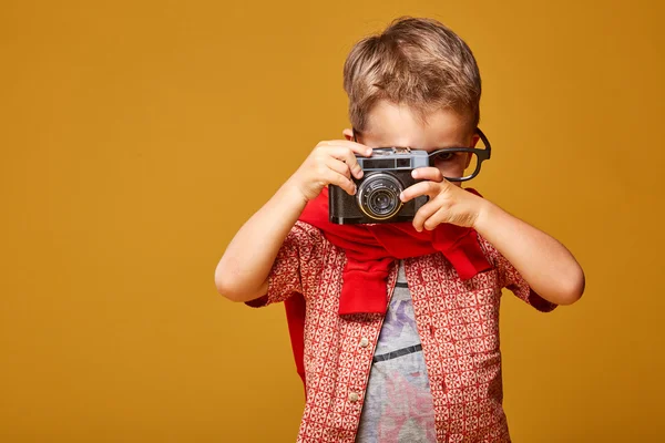 Little boy with camera in studio with yellow background