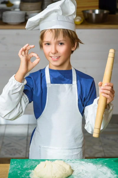 Funny happy chef boy cooking at restaurant kitchen or holding the dough and showing Ok