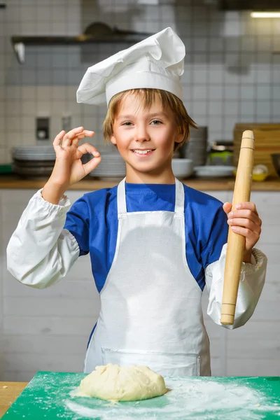 Funny happy chef boy cooking at restaurant kitchen or holding the dough and showing Ok