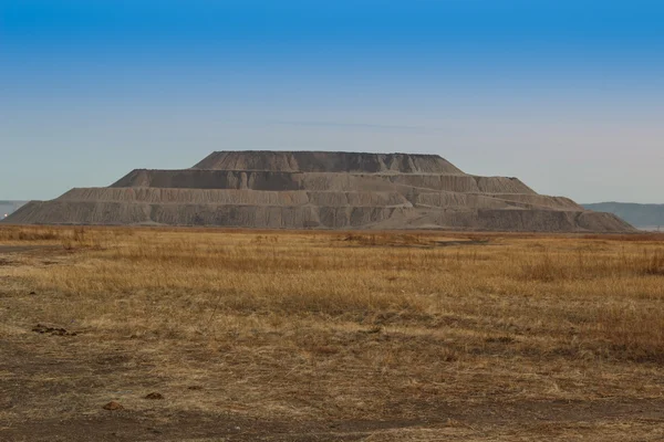 Industrial pyramid of earth extracted in the quarry. Mountain waste rock in the shape a pyramid.