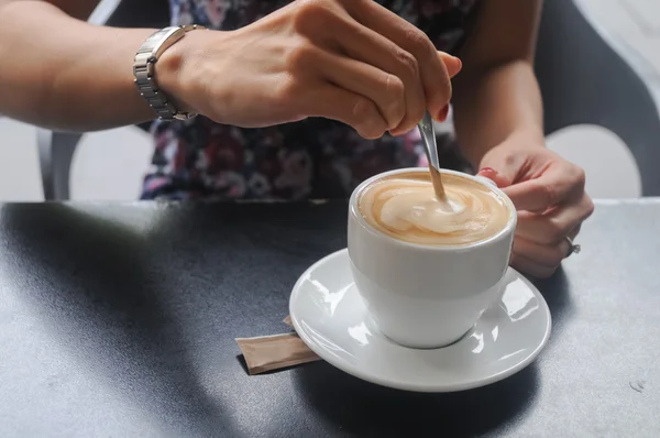 A lady hand stirring fresh brewed morning coffee on a black table