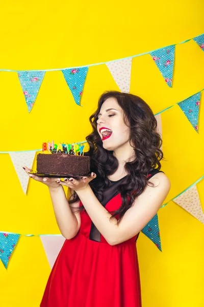 Beautiful caucasian girl blowing candles on her cake. Celebration and party. Having fun. Young pretty woman in red dress and birthday hat is laughing.