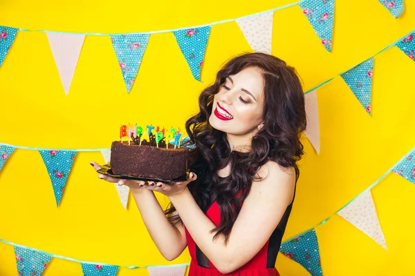 Beautiful caucasian girl blowing candles on her cake. Celebration and party. Having fun. Young pretty woman in red dress and birthday hat is laughing.