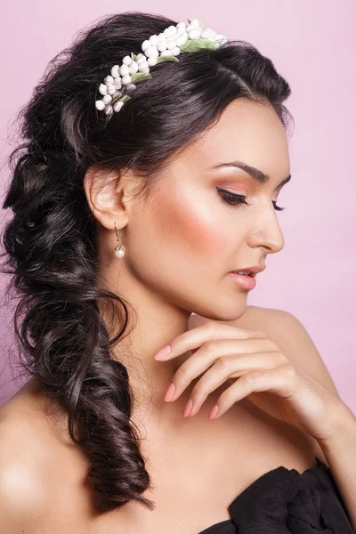 Beautiful young girl with a floral ornament in her hair on a pink background. Woman with Perfect Makeup.