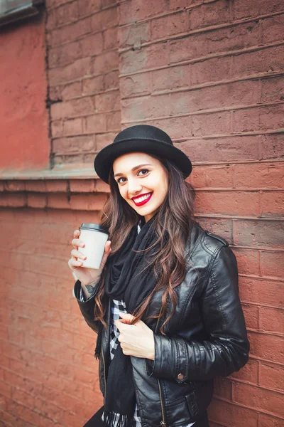 Trendy woman in hat  with drink outdoor. Young  woman with red lips  in the street and holding cup of coffee